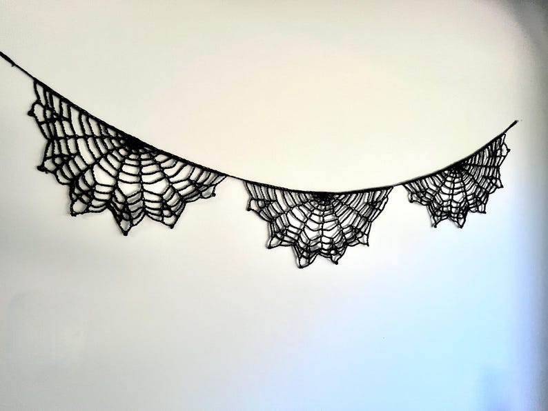 Op de afbeelding: Zwarte spinnenweb slinger, perfect voor Halloween-decoraties. De slinger heeft drie spinnenweb ontwerpen die zijn verbonden door een dun zwart touwtje. De spinnenwebben hebben een gedetailleerd, ingewikkeld ontwerp.