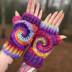 Puede incluir: Un par de guantes sin dedos de ganchillo coloridos con un patrón en espiral en tonos de morado, naranja, amarillo y azul.