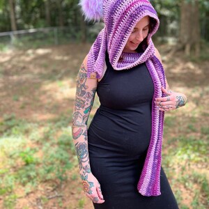 May include: A purple and pink striped hooded scarf with fuzzy earmuffs. The scarf is crocheted and has a long, flowing design.