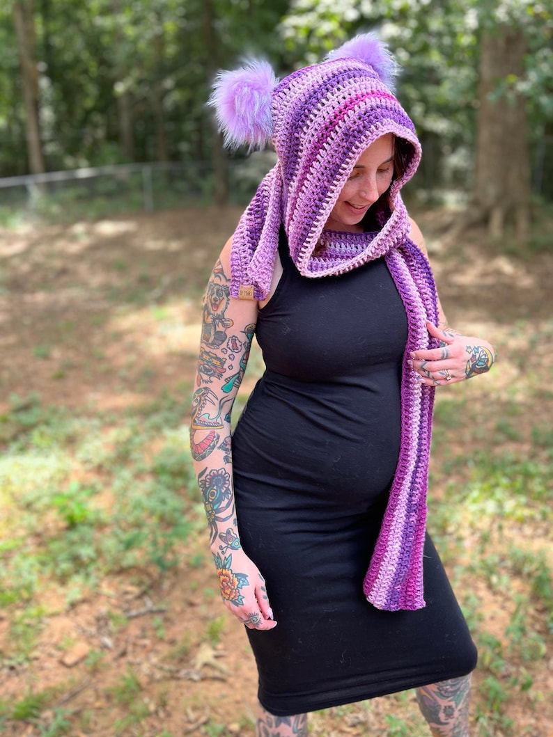 May include: A purple and pink striped hooded scarf with fuzzy earmuffs. The scarf is crocheted and has a long, flowing design.