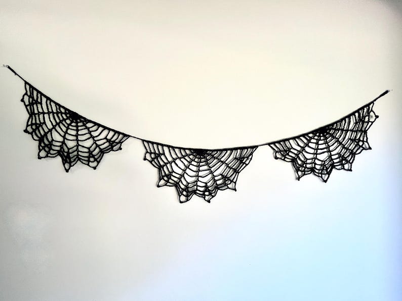 Op de afbeelding: Een zwarte spinnenweb slinger, ideaal voor Halloween decoraties. De slinger heeft drie web ontwerpen verbonden door een dun zwart touwtje. De webben zijn ingewikkeld ontworpen met een gedetailleerd patroon, wat een spookachtige uitstraling cre&euml;ert.