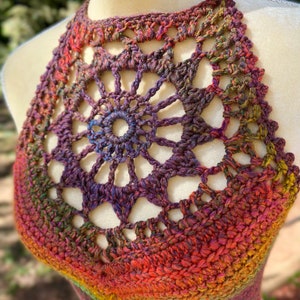 May include: A crocheted halter top with a colorful ombre design in shades of red, orange, yellow, green, purple, and brown. The top features a large, openwork mandala design in the center.