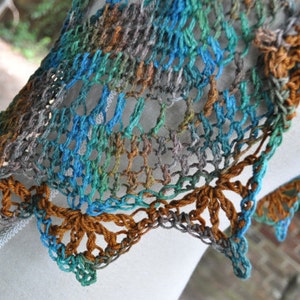 May include: A crocheted shawl in shades of brown, blue, and green. The shawl has a delicate lace pattern and a scalloped edge.