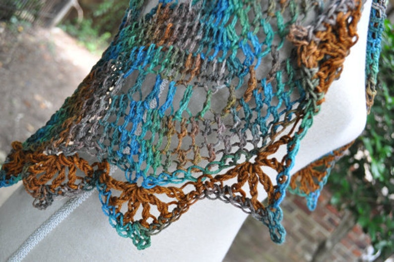May include: A crocheted shawl in shades of brown, blue, and green. The shawl has a delicate lace pattern and a scalloped edge.