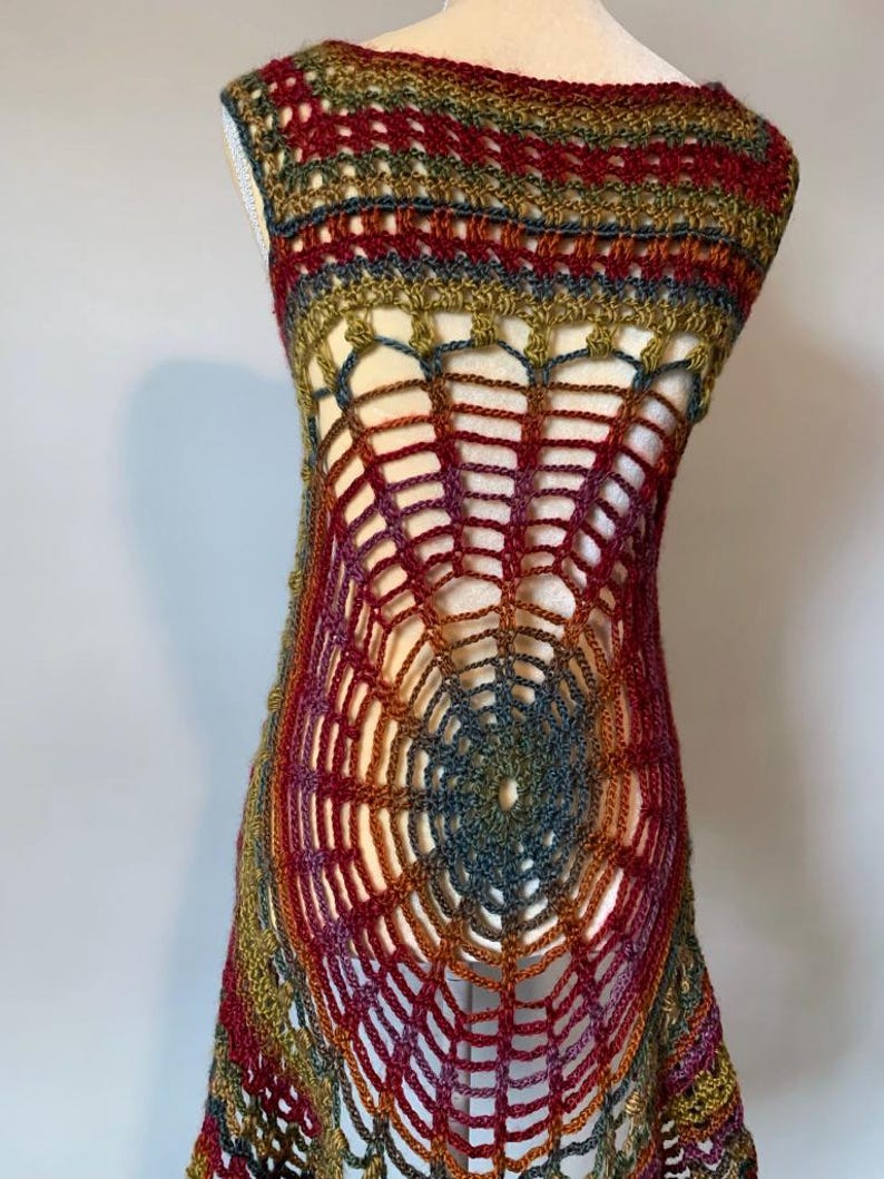 May include: A sleeveless crochet tunic featuring a prominent spiderweb pattern in the center. The garment is crafted from variegated yarn in shades of deep red, olive green, gold, and dark blue, creating a textured, open-work design.