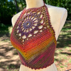 May include: A crocheted halter top with a rainbow ombre color pattern. The top features a large crocheted flower design at the neckline.