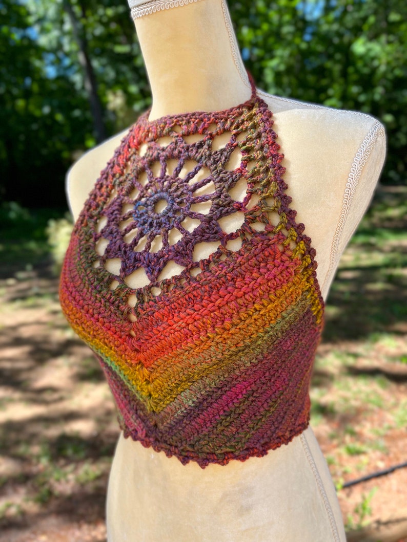 May include: A crocheted halter top with a rainbow ombre color pattern. The top features a large crocheted flower design at the neckline.