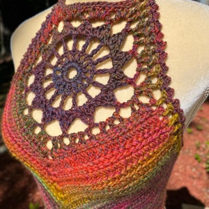 May include: A crocheted halter top with a colorful ombre design. The top features a large, openwork circle in the center.