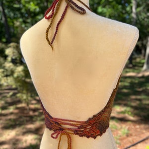 May include: A crocheted halter top with a brown, orange, and red color gradient. The top has a lace-up back and a halter neck style.