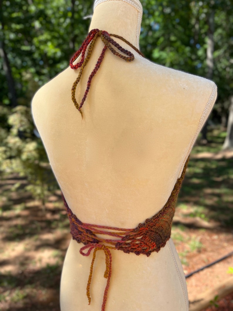 May include: A crocheted halter top with a brown, orange, and red color gradient. The top has a lace-up back and a halter neck style.