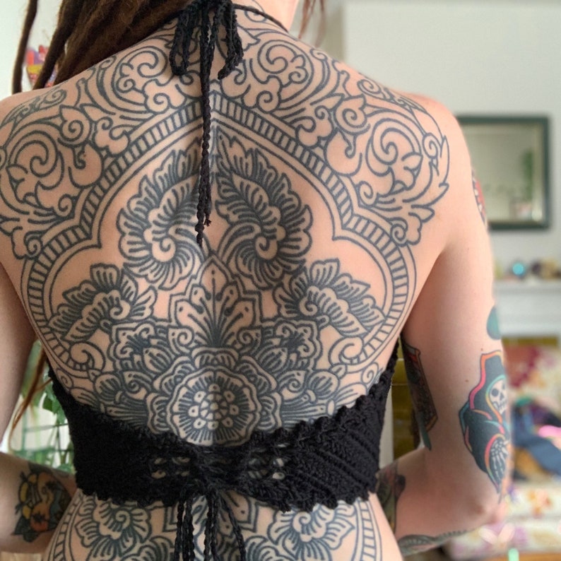 Puede incluir: Una persona con un gran tatuaje de mandala negro y blanco en la espalda, usando un top de crochet negro.