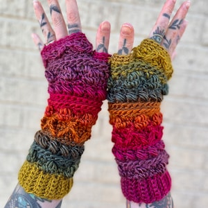May include: A pair of colorful crocheted fingerless gloves with a gradient of red, orange, yellow, and green. The gloves are made with a textured stitch and have a warm, cozy look.