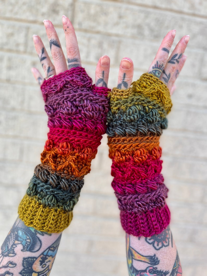 May include: A pair of colorful crocheted fingerless gloves with a gradient of red, orange, yellow, and green. The gloves are made with a textured stitch and have a warm, cozy look.