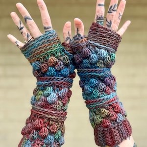 May include: A pair of colorful crocheted fingerless gloves with a textured, bubble-like design. The gloves are made with a variety of shades of blue, green, brown, and red yarn.