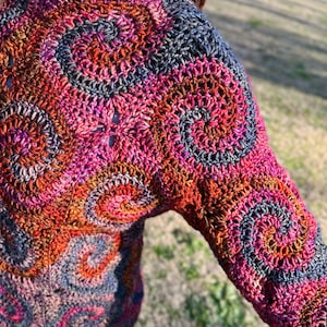 May include: A colourful crochet sweater with a circular pattern in shades of pink, orange, brown, and grey.