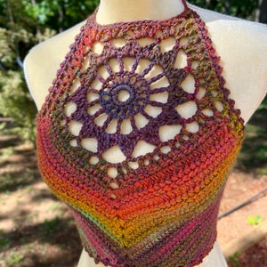 May include: A crocheted halter top with a rainbow ombre color pattern. The top features a large, openwork, circular design in the center.