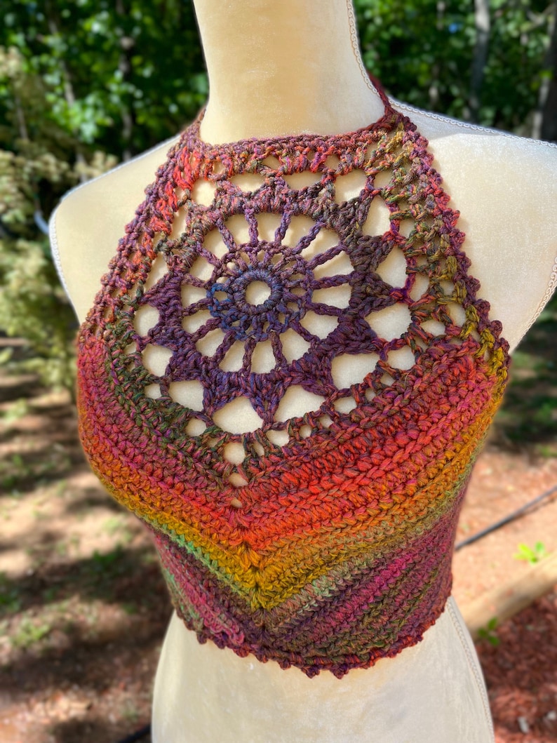 May include: A crocheted halter top with a rainbow ombre color pattern. The top features a large, openwork, circular design in the center.