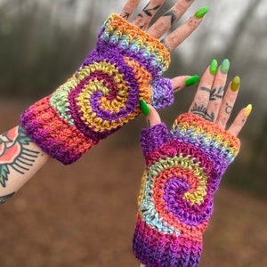 Może przedstawiać: Para kolorowych, szydełkowych rękawiczek bez palc&oacute;w ze spiralnym wzorem w odcieniach fioletu, pomarańczy, ż&oacute;łci i zieleni.