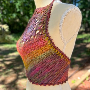 May include: A crocheted halter top with a colorful ombre design in shades of red, orange, yellow, green, and purple. The top has a delicate crocheted pattern and a halter neckline.