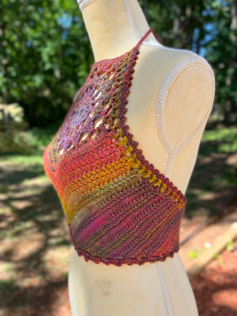 May include: A crocheted halter top with a colorful ombre design in shades of red, orange, yellow, green, and purple. The top has a delicate crocheted pattern and a halter neckline.