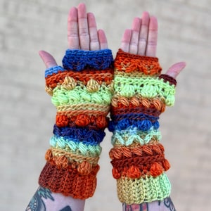 May include: A pair of colorful crocheted fingerless gloves with a multi-colored striped pattern. The gloves feature a variety of stitches and textures, including bobbles and raised stitches.