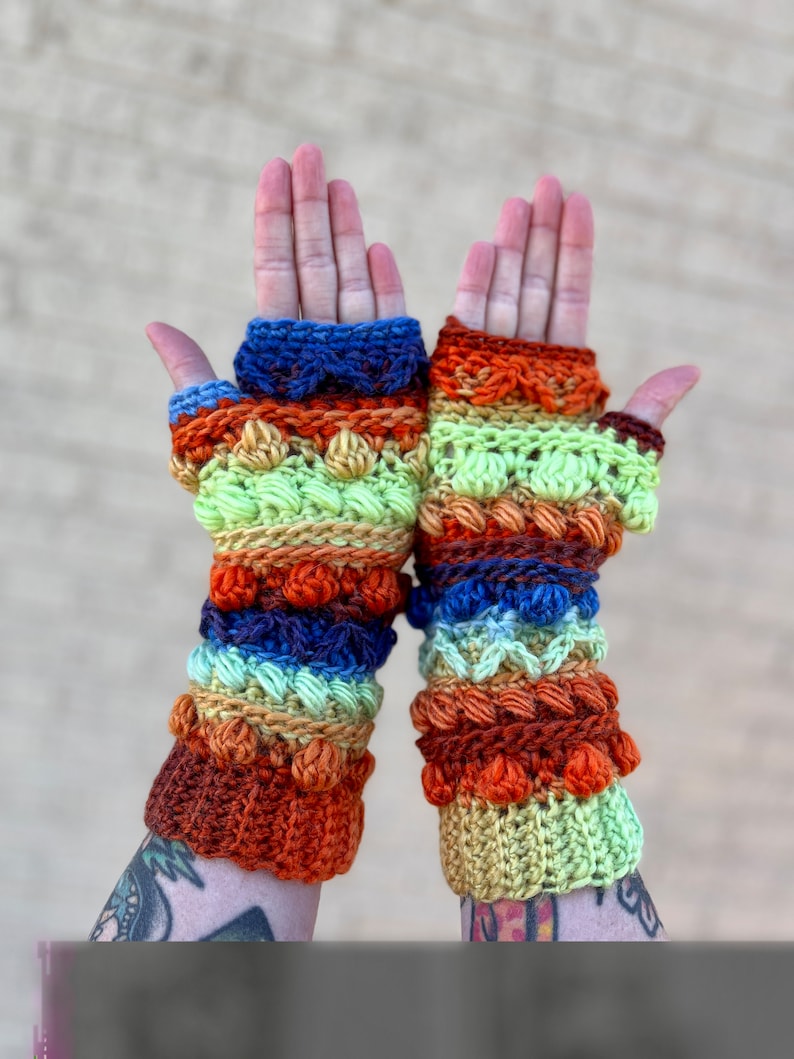 May include: A pair of colorful crocheted fingerless gloves with a multi-colored striped pattern. The gloves feature a variety of stitches and textures, including bobbles and raised stitches.