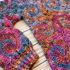 May include: A crocheted sweater with a colourful swirl pattern in shades of pink, purple, orange, and brown.