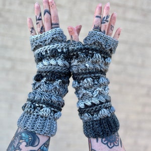 May include: A pair of gray and black fingerless crochet gloves with a textured design. The gloves are made with a variety of stitches and yarns, creating a unique and stylish look.