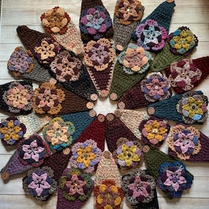 May include: A collection of triangular crochet headbands arranged in a circular pattern. Each headband features a textured knit base in various solid colors and is adorned with a multi-layered, multi-colored crochet flower and a button.
