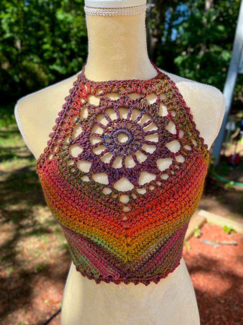 May include: A crocheted halter top with a colorful ombre design in shades of red, orange, yellow, green, and purple. The top features a large crocheted flower design at the neckline.