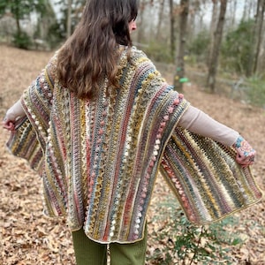 May include: A white ceramic mug with a black handle and the text "But First, Coffee" in a bold, black font. The mug is set against a blurred background, suggesting a cozy setting.