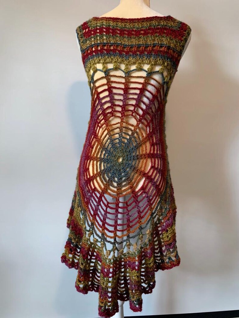 May include: A sleeveless crochet tunic featuring a prominent spiderweb pattern in the center. The garment is crafted from variegated yarn in shades of deep red, olive green, and muted blue, with a flared, scalloped hemline and an open-work design.