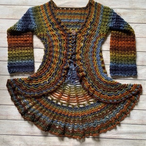 May include: A long-sleeved crochet cardigan featuring a multi-coloured gradient pattern in shades of blue, green, orange, and brown. The garment has a lace-like openwork texture, a V-neckline, and a centre front lace-up closure with matching yarn ties.