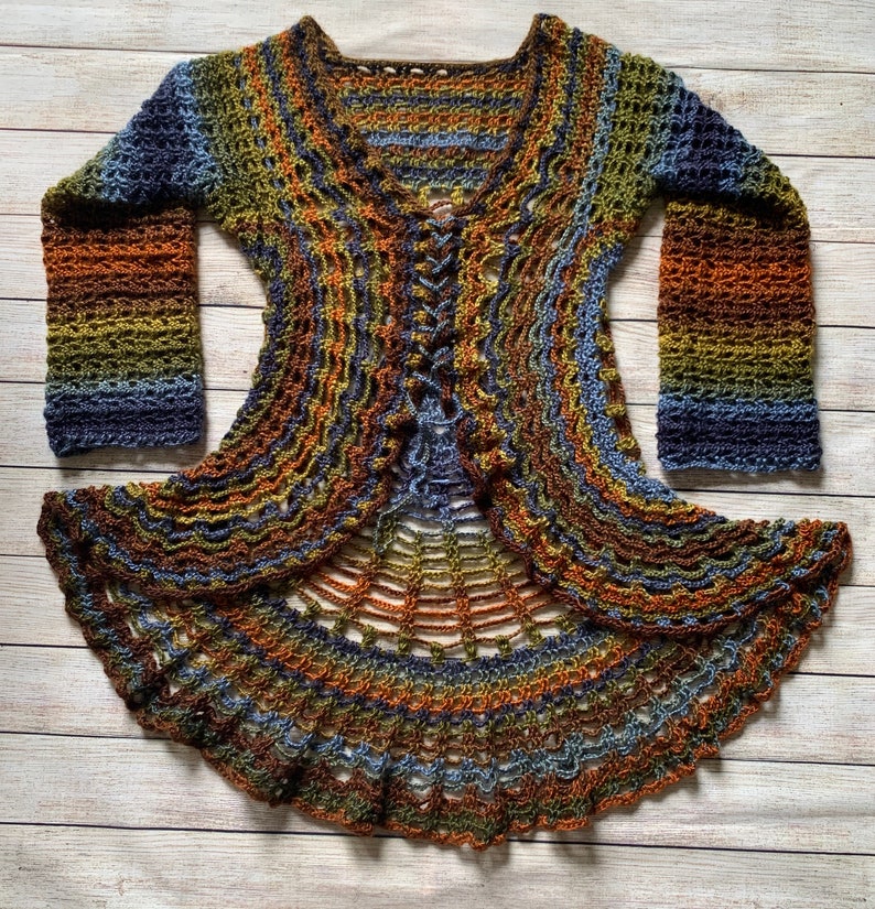 May include: A long-sleeved crochet cardigan featuring a multi-coloured gradient pattern in shades of blue, green, orange, and brown. The garment has a lace-like openwork texture, a V-neckline, and a centre front lace-up closure with matching yarn ties.