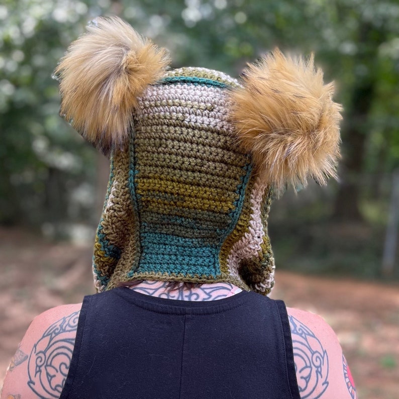 May include: A crocheted hooded hat with faux fur ear flaps. The hat is green, brown, and beige with a striped pattern.