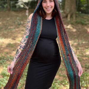 May include: A crocheted hooded scarf with a multi-colored striped pattern in shades of orange, teal, and brown. The scarf has a hood with two fluffy white ear-like accents.