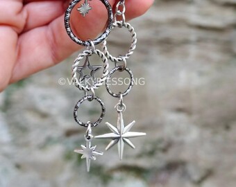 May include: A pair of silver-toned dangle earrings featuring interconnected rings with textured and twisted metal finishes. The earrings incorporate star-shaped charms of varying sizes and include the text VALKYRIESSONG printed on the metal surface.