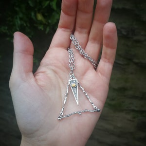 May include: A silver necklace with a triangular pendant featuring a small, iridescent gemstone. The pendant is made of twisted wire and has a delicate, intricate design.
