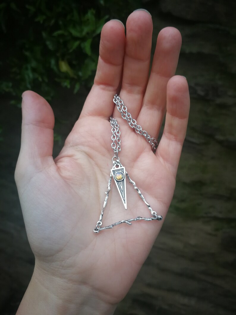 May include: A silver necklace with a triangular pendant featuring a small, iridescent gemstone. The pendant is made of twisted wire and has a delicate, intricate design.