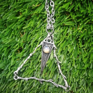 May include: A silver necklace with a triangle pendant featuring a small iridescent gemstone. The pendant is made of branches with a delicate design.