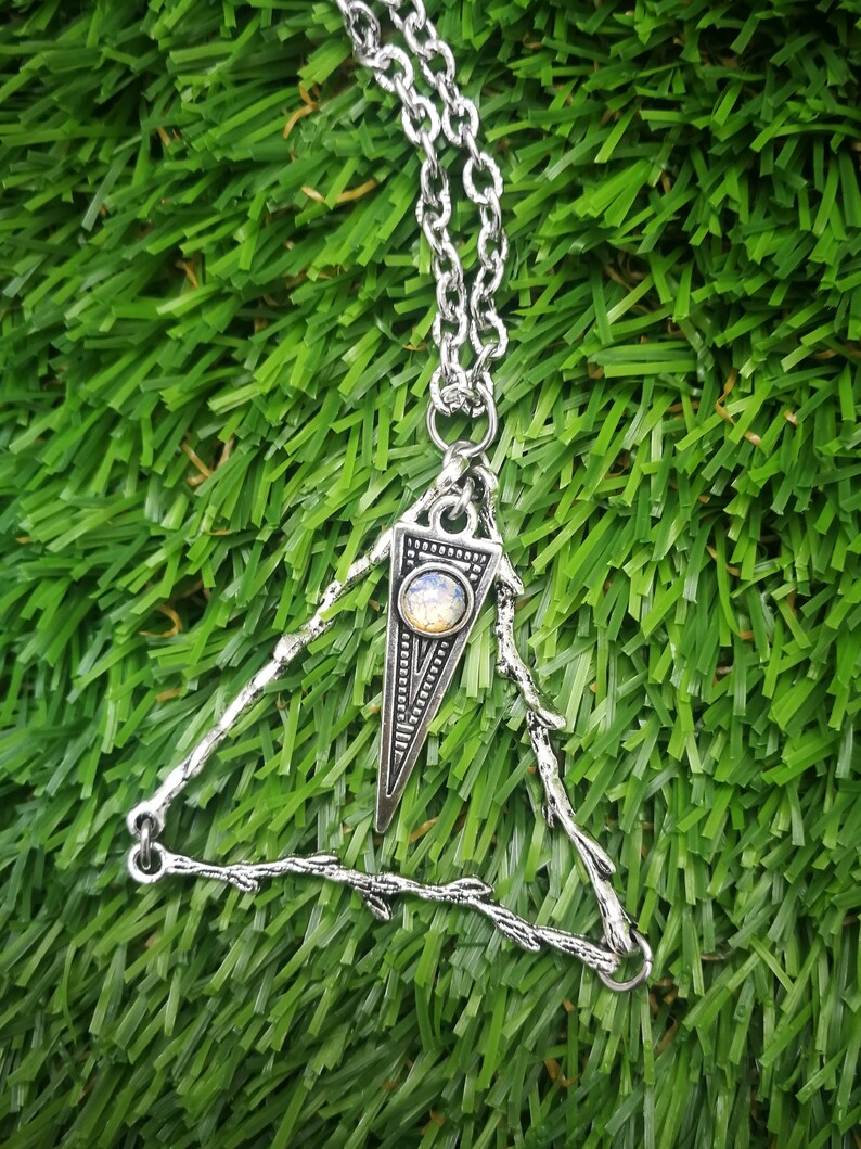 May include: A silver necklace with a triangle pendant featuring a small iridescent gemstone. The pendant is made of branches with a delicate design.