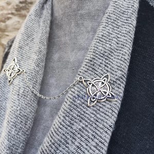 May include: A silver chain with two Celtic knot designs, one on each end. The chain is draped over a gray sweater.