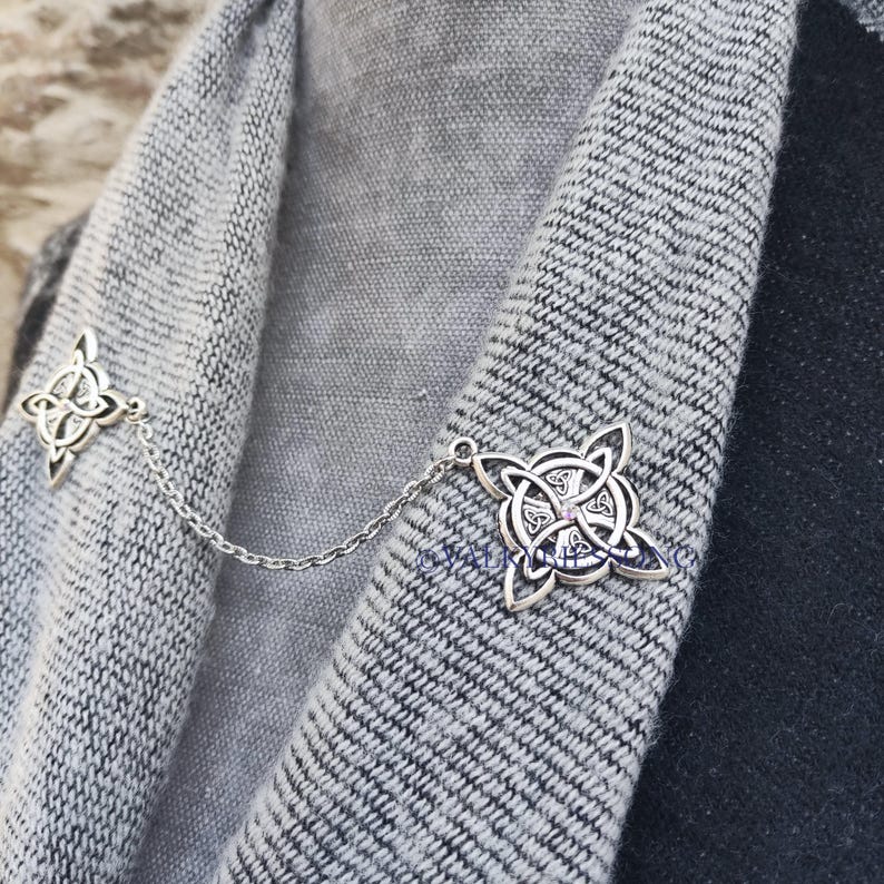 May include: A silver chain with two Celtic knot designs, one on each end. The chain is draped over a gray sweater.