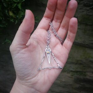 May include: A silver necklace with a triangular pendant featuring a small, round, yellow gemstone. The pendant is made of twisted wire.