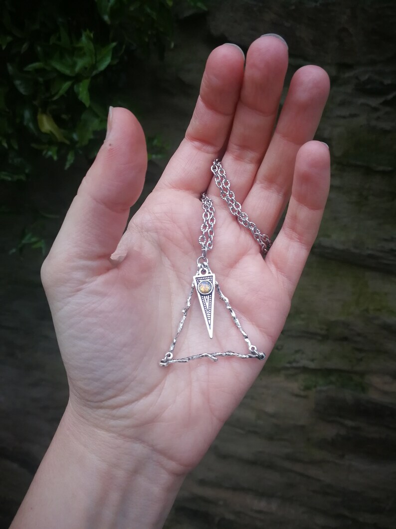 May include: A silver necklace with a triangular pendant featuring a small, round, yellow gemstone. The pendant is made of twisted wire.