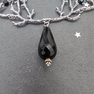May include: A silver-toned necklace featuring a branch-like design with small black beads and a faceted black teardrop pendant. The necklace has a delicate chain and a star-shaped charm.
