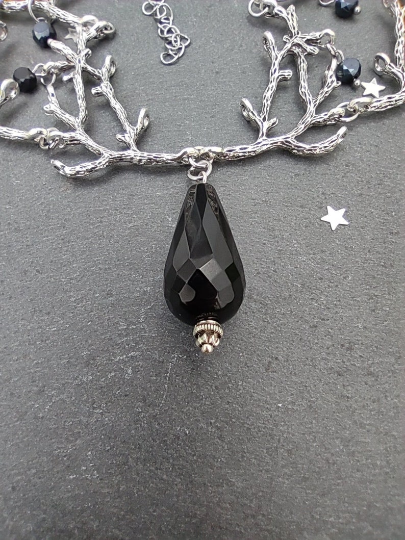 May include: A silver-toned necklace featuring a branch-like design with small black beads and a faceted black teardrop pendant. The necklace has a delicate chain and a star-shaped charm.