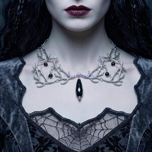 Handmade silver metal branch necklace with a faceted black onyx teardrop pendant. The intricate gothic fantasy design features silver-toned coral or twig-like structures adorned with small black gemstone beads, creating a statement nature-inspired, ethereal gothic look.