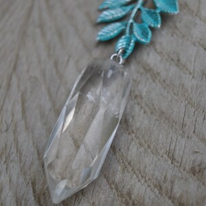 May include: A clear quartz crystal pendant necklace with a faceted, elongated shape. The pendant hangs from a silver chain with a turquoise-coloured leaf design. The necklace features a strand of pink and white beads.