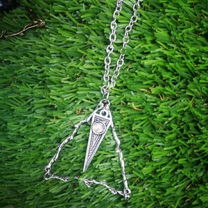 May include: A silver necklace with a triangular pendant featuring a clear gemstone. The pendant is made of intricate metalwork and has a delicate, bohemian style.